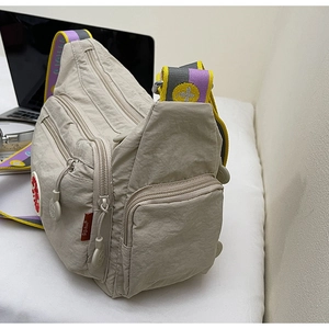 Macro detail of beige nylon crossbody bag with four zipper pockets and woven bee strap