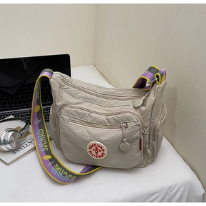 Detail of beige nylon crossbody bag with multiple zip pockets and purple-yellow strap