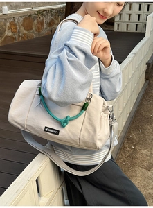 Scatto lifestyle di una borsa in nylon crema con nodo verde e dettaglio etichetta nera