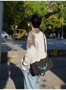 Foto all'aperto di una borsa a tracolla in nylon nero con manico intrecciato verde acqua
