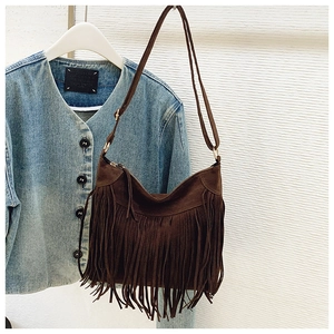 Detail of dark brown suede hobo bag with long fringes styled on a denim jacket