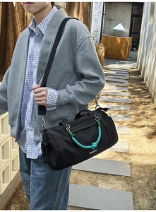 Dettaglio borsa cilindrica in nylon nero con manici intrecciati blu e accenti verdi