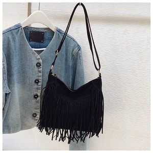 Detail of black faux suede shoulder bag featuring long fringe tassels and zipper closure