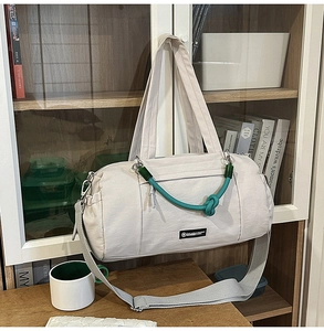 Dettaglio borsa da viaggio in nylon crema con manici in corda verde su un mobile