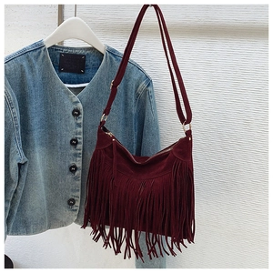 Detail of burgundy suede tote bag featuring long decorative tassels and adjustable strap