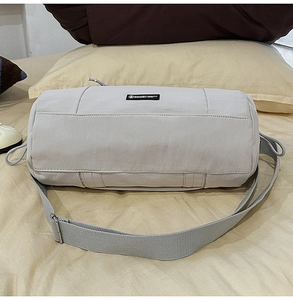 Dettaglio borsa a cilindro in nylon grigio chiaro con tracolla regolabile e logo