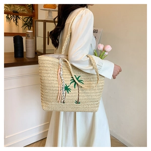 Detail of beige straw tote bag featuring green palm tree embroidery and fringe tassel