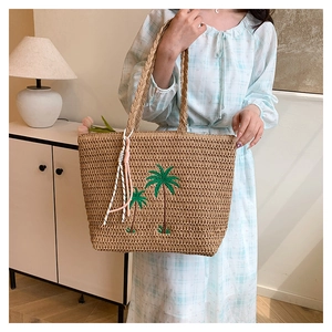 Detail of straw tote bag featuring green palm tree embroidery and pink tassel charm