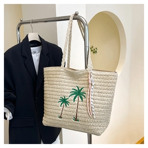 Detail of beige straw tote bag featuring green coconut tree embroidery and rope charm