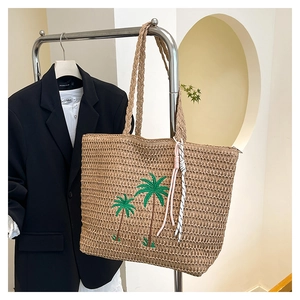 Close-up of beige straw beach bag featuring green palm tree embroidery and woven handles