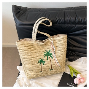 Detail of straw tote bag featuring green coconut tree embroidery and colorful rope charms