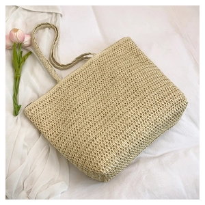 Detail of a large capacity straw tote bag with braided handles on white fabric
