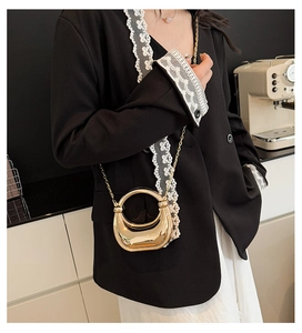 Detailed close-up of a hollow circular gold metal handbag with a mirror finish and chain