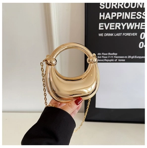 Detail of a crescent gold mirror-finish mini bag with ring handle and fine chain