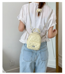 Detail of a light yellow quilted mini backpack with metal chain straps and a twist lock