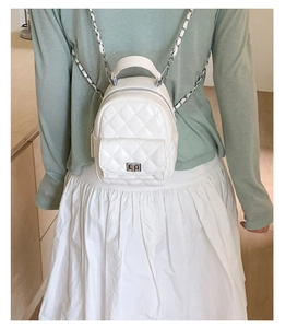 Detail of white quilted mini backpack with chain strap and twist lock on a model
