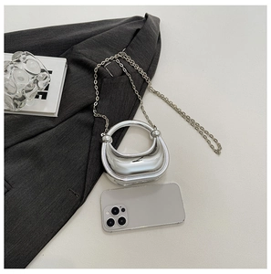 Mini silver crescent acrylic evening bag with metal chain shown next to a smartphone