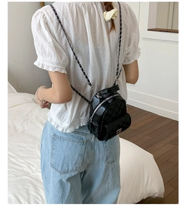 Rear view of a model wearing a mini black quilted backpack with silver chain straps