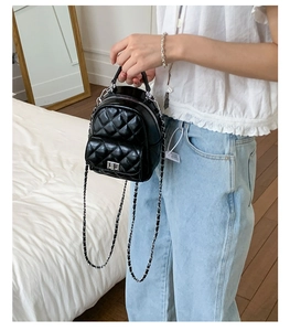 Close-up of mini black quilted leather backpack with silver lock and chain strap