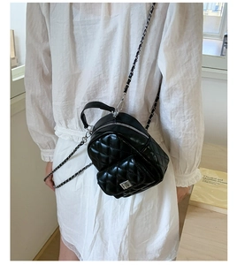 Detail of black quilted mini backpack with silver chain strap and metal clasp closure