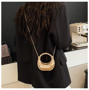 Close-up of golden crescent acrylic clutch with round handle and metallic chain strap