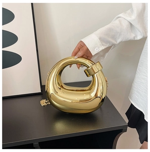 Detailed view of the mirrored gold metal donut-shaped evening clutch with its chain strap