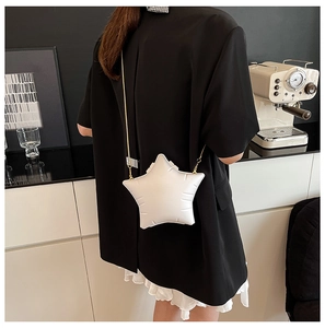 Detail of white star-shaped padded crossbody bag with gold chain on model in black blazer
