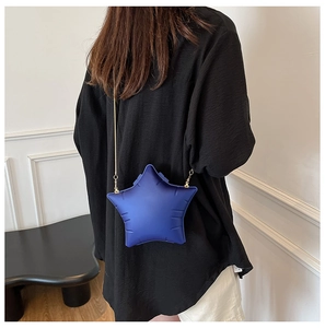Close-up of blue star-shaped crossbody bag with gold chain strap on a model outfit
