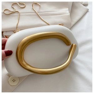 Detail of white PU leather clutch with artistic golden C-shaped handle and chain
