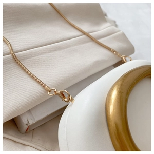 Detailed shot of golden metal handle and snake chain on a white leather handbag