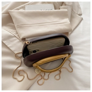 Detail of dark brown structured handbag featuring a gold curved metal handle and chain