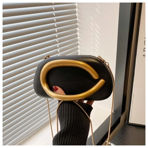 Detail of black oval clutch featuring a bold gold curved handle and sleek snake chain strap
