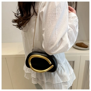 Detail of black oval crossbody bag with gold C-shaped metal clasp and chain strap