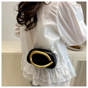 Close-up of elegant black evening bag with a large gold C-shaped metal clasp and chain