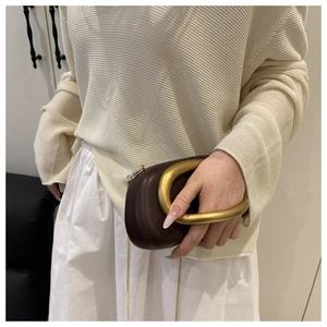 Detail of dark brown leather clutch featuring a chunky gold metal horseshoe handle
