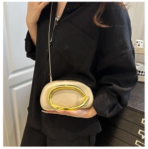 Close-up of champagne acrylic evening clutch with large C-shaped gold metal handle and chain