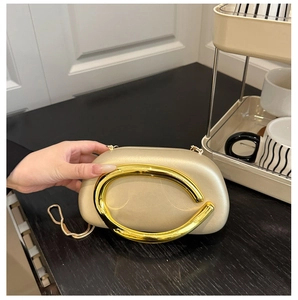 Detail of round champagne acrylic clutch featuring a large oval gold metal handle and chain