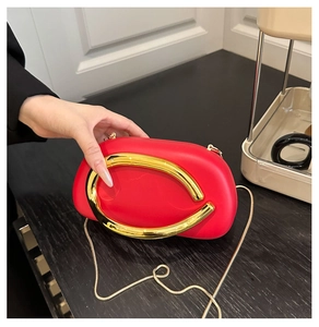 Detail of red acrylic round clutch with gold C-handle and delicate snake chain strap