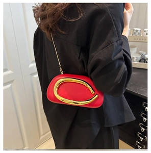 Detail of red acrylic dinner bag with sculptural gold C-handle and metal chain strap