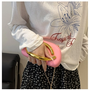 Detailed view of pink acrylic clutch with large gold U-shaped handle and sleek finish