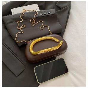 Brown round evening bag with a unique gold metal handle beside a smartphone for scale