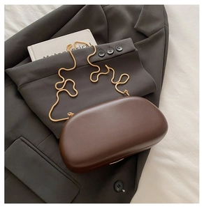 Flat lay of a brown capsule evening clutch with gold snake chain on a gray blazer