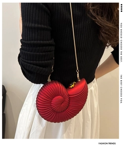 Detailed view of a red seashell clutch with gold chain strap on a stylish model