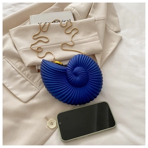 Detail view of navy blue conch shell clutch with gold chain on a beige blazer
