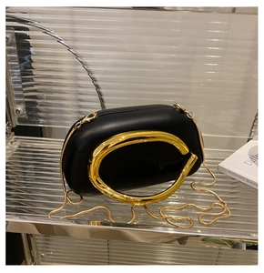 Detail of black acrylic evening bag featuring large gold C-shaped metal handle and chain