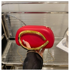Detail of red acrylic evening bag with large gold C-shaped metal handle and chain