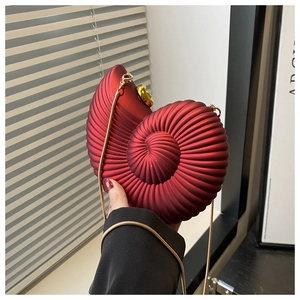 Detail of red conch-shaped evening bag with gold chain and spiral texture held by model