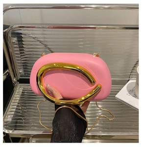 Detail of pink acrylic clutch with round gold metal handle and crossbody chain strap