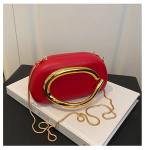 Detail of red acrylic evening clutch bag with C-shaped gold metal handle and chain strap