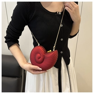 Close-up of a red seashell evening clutch with a gold chain strap on a black outfit
